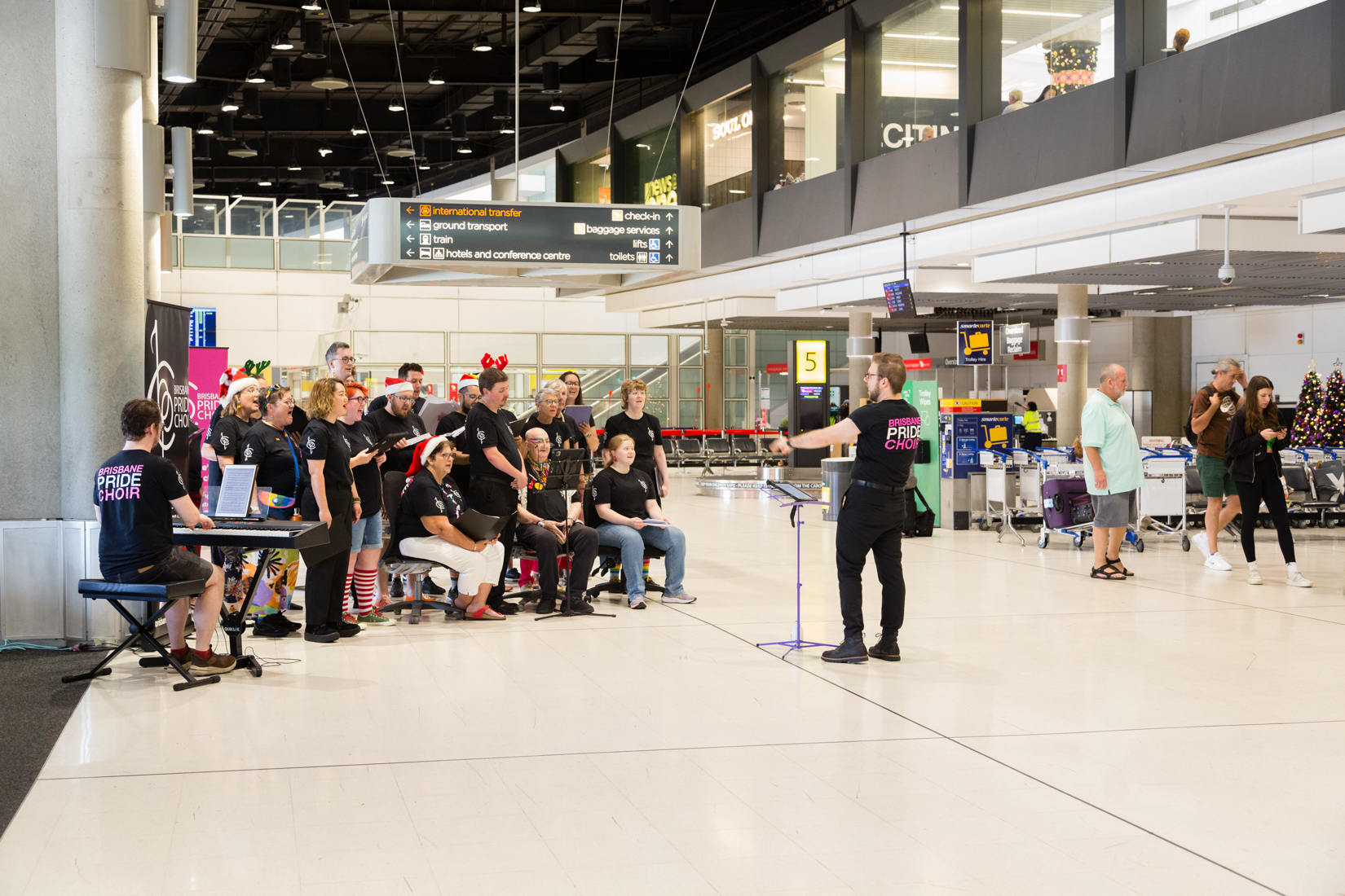 Brisbane Pride Choir performing inside the Brisbane Domestic Terminal with passengers watching them